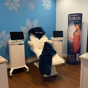 Spa treatment chair with white upholstery and dark blue towels, flanked by two equipment carts in a blue snowflake-themed room with monitors on them.